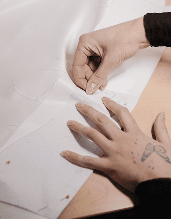 Close up of hands carefully pinning white lace fabric on a wedding gown