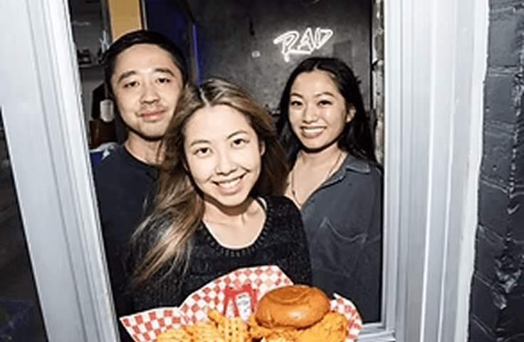 Group of three smiling volunteers holding packed meals for the community in need