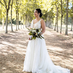 Bride holding a bouquet in a forest wearing a perfectly fitted wedding gown